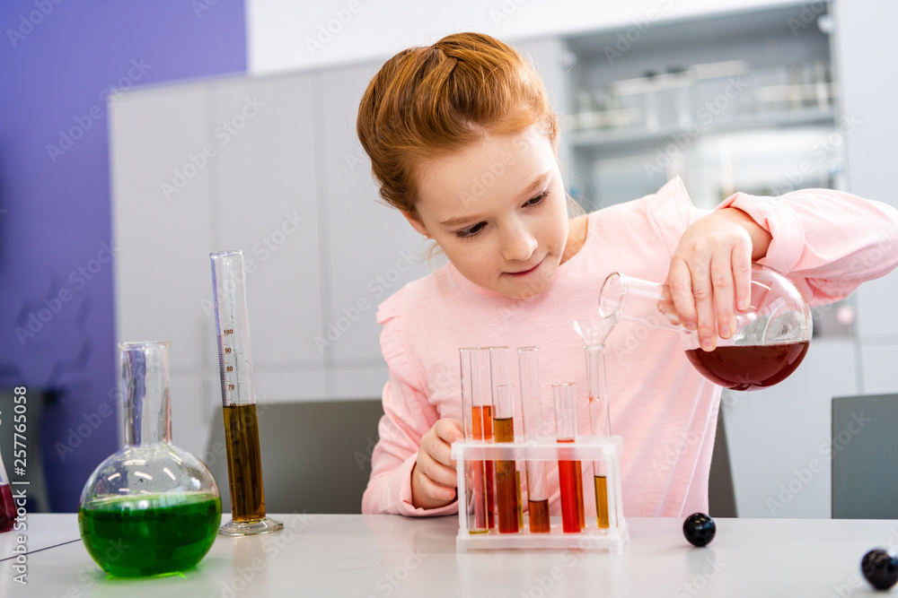 Smiling schoolgirl holding beaker and doing chemical experiment during chemistry lesson Smiling schoolgirl holding beaker and doing chemical experiment during chemistry lesson