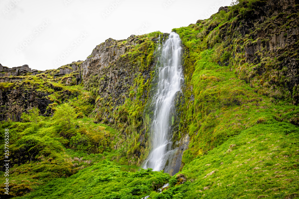 Small waterfall by Seljalandsfoss, Iceland with white water falling off cliff top long exposure in green mossy summer rocky landscape Small waterfall by Seljalandsfoss, Iceland with white water falling off cliff top long exposure in green mossy summer rocky landscape