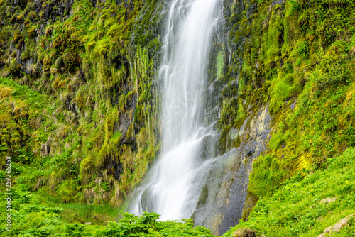 Small waterfall closeup by Seljalandsfoss, Iceland with white water falling off cliff top long exposure in green mossy summer rocky landscape