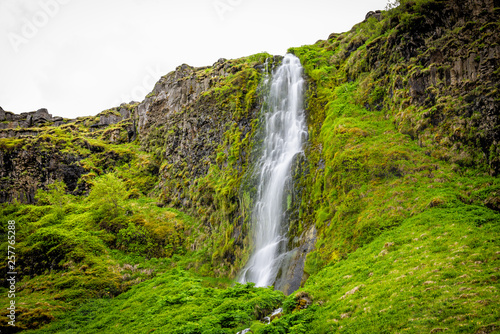 Small waterfall by Seljalandsfoss  Iceland with white water falling off cliff top long exposure in green mossy summer rocky landscape