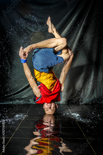 cool and happy korean young guy break dancer in style of bboying doing complex tricks on floor with water splashes and liquid drops effects in aqua zone photo studio with black isolated background photo