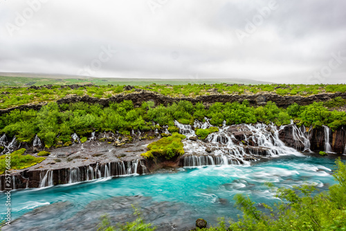 Colorful blue aqua turquoise vibrant color water waterfall azure cascades Hraunfossar Lava Falls in Iceland with rainy cloudy landscape view