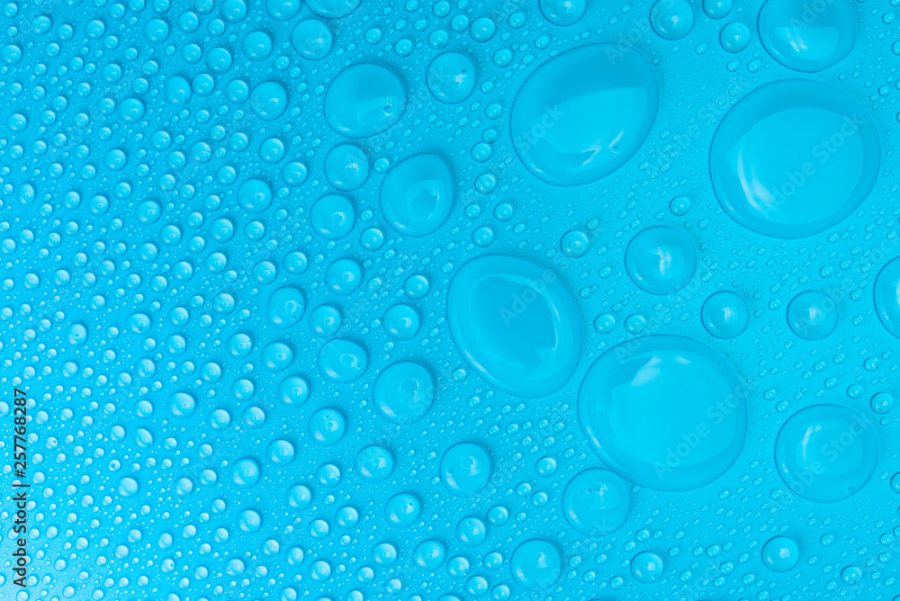 Droplets of water on a blue, matte background illuminated with a delicate light.