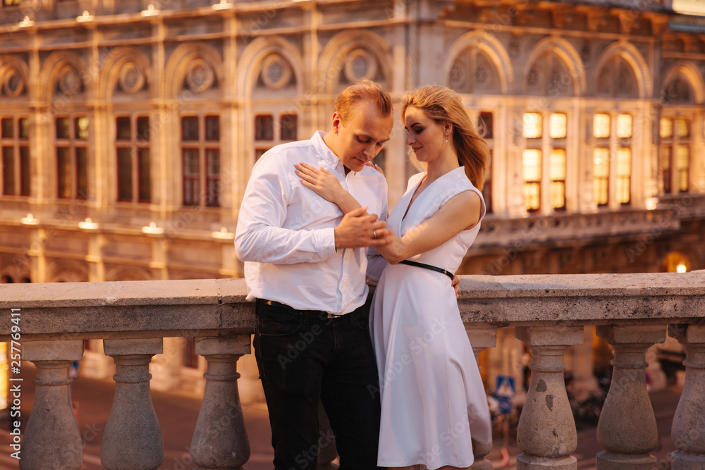 Obraz premium Happy woman and man in white clothes stand by the border in front of city view. City illuminated