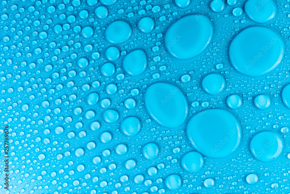Droplets of water on a blue, matte background illuminated with a delicate light.