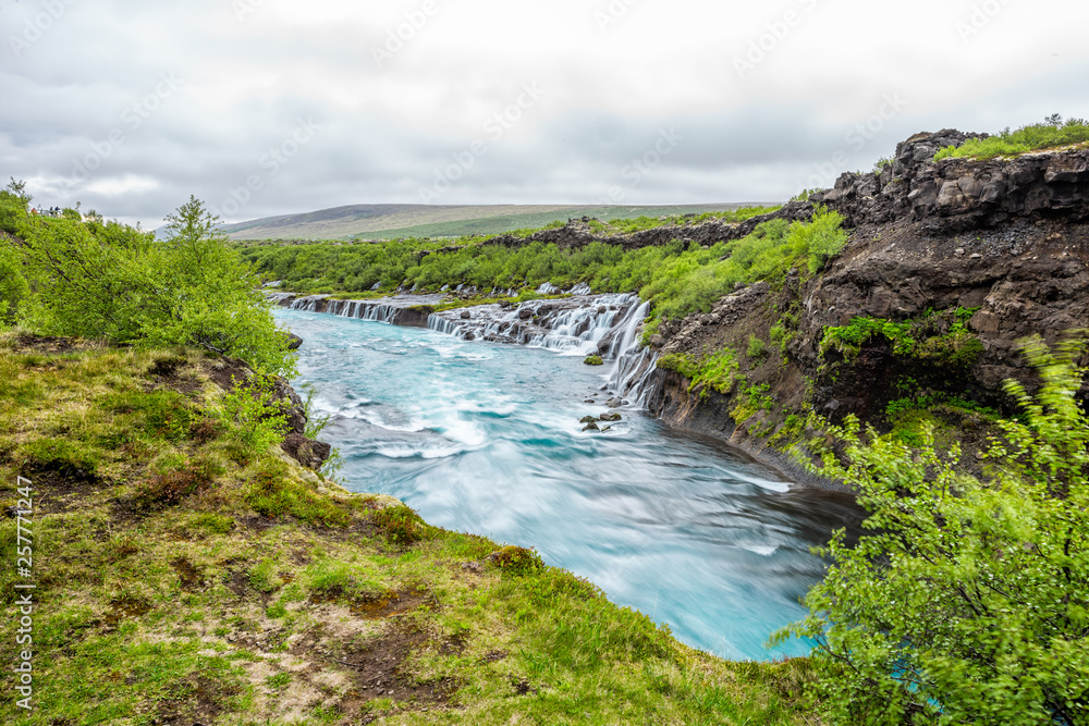 Long exposure smooth colorful vibrant blue aqua turquoise water waterfall cascades Hraunfossar Lava Falls in Iceland, landscape view