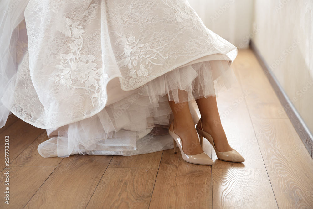 Bride putting on wedding shoes at home where she's getting ready - Wearing white dress in a bright room with wooden floor Bride putting on wedding shoes at home where she's getting ready - Wearing white dress in a bright room with wooden floor