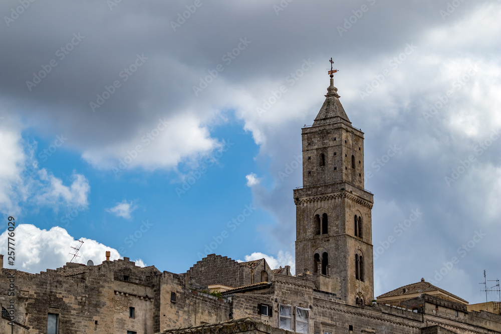 Summer blue sky and church roof with religious cross, view of ancient town of Matera, the Sassi di Matera, Basilicata, Southern Italy, cloudy summer August day