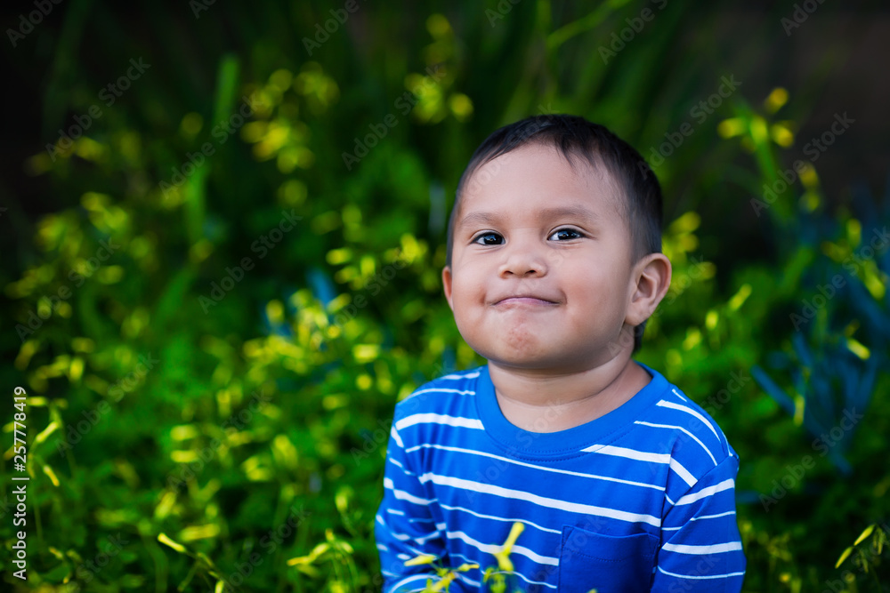 A healthy boy looking up in admiration with a positive attitude and satisfied smile sitting in a field of yellow wild flowers while wearing a striped blue shirt. A healthy boy looking up in admiration with a positive attitude and satisfied smile sitting in a field of yellow wild flowers while wearing a striped blue shirt.
