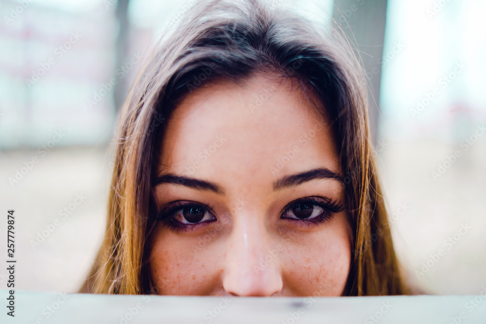 Close up on young woman's eyes hiding her face behind the table in park Close up on young woman's eyes hiding her face behind the table in park