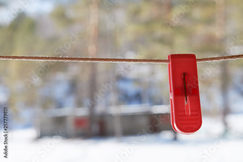 red plastic clothespin hanging on a clothesline in the yard in the spring against a blurred background