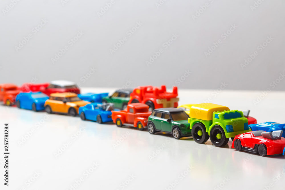 Plastic multi-colored toy cars are lined up on a white background. Stereotypical alignment of subjects is a sign of autism. Selective focus. Copy space for text. Traffic jams air pollution concept. Plastic multi-colored toy cars are lined up on a white background. Stereotypical alignment of subjects is a sign of autism. Selective focus. Copy space for text. Traffic jams air pollution concept.