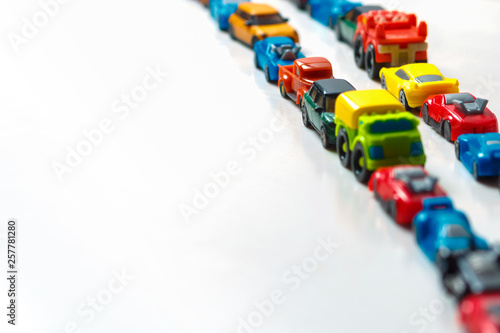 Plastic multi-colored toy cars are lined up on a white background. Stereotypical alignment of subjects is a sign of autism. Selective focus. Copy space for text. Traffic jams air pollution concept.