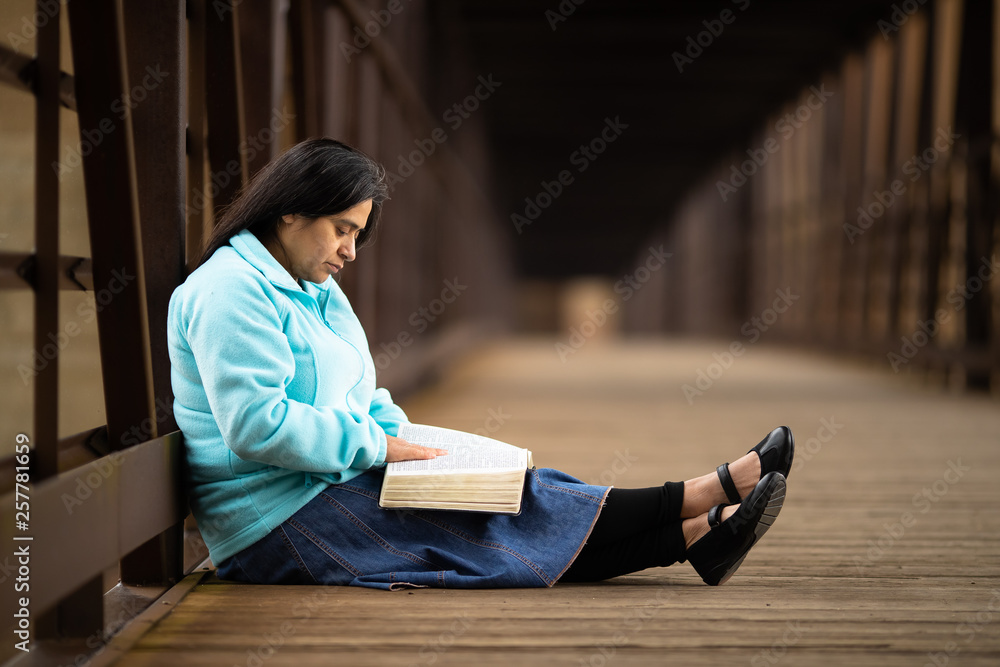 Hispanic Woman Sitting And Reading Bible On A Bridge Hispanic Woman Sitting And Reading Bible On A Bridge