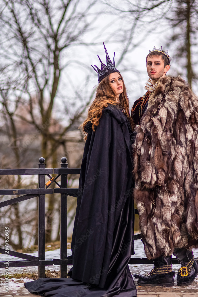 Art Photography and Cosplay.Caucasian Couple as King and Queen in Fur Medieval Outfit With Crowns Posing Together Outdoors.