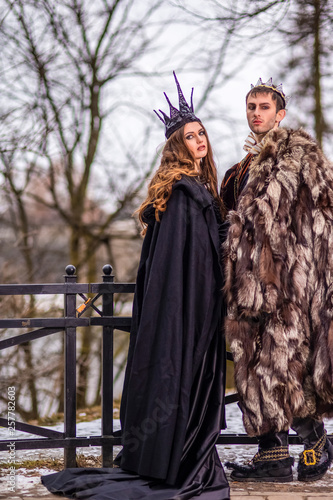 Art Photography and Cosplay.Caucasian Couple as King and Queen in Fur Medieval Outfit With Crowns Posing Together Outdoors.