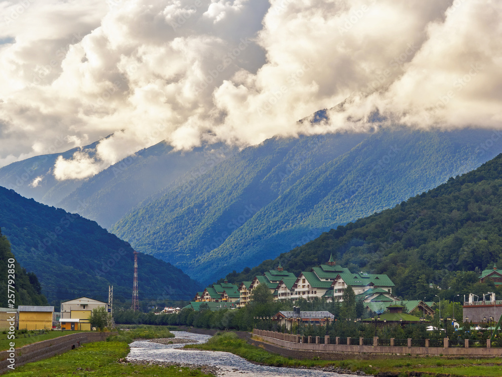 The river flows between the green mountains in front of the complex of hotels.