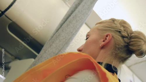 Low angle shot of beautiful elegant blonde stewardess demonstrating passengers on a board how to put on a safety mask. Pre-flight rules, professional, profession concept. Travelling