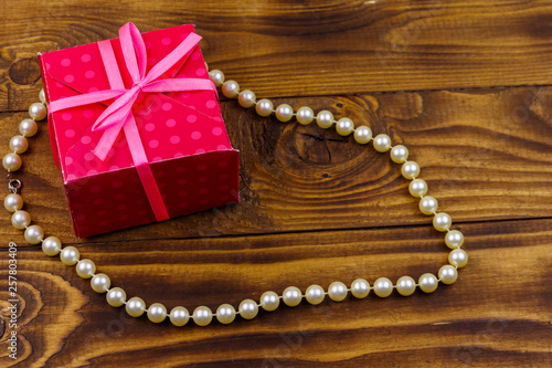 Gift box and pearl necklace on wooden background