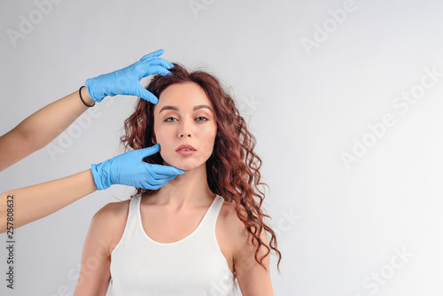 Cosmetologist checking out face of a woman with hands in gloves isolated over white background