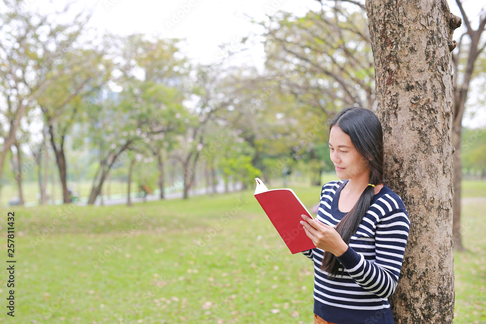 Young woman reading a book standing lean against trunk tree in summer park outdoor. Young woman reading a book standing lean against trunk tree in summer park outdoor.