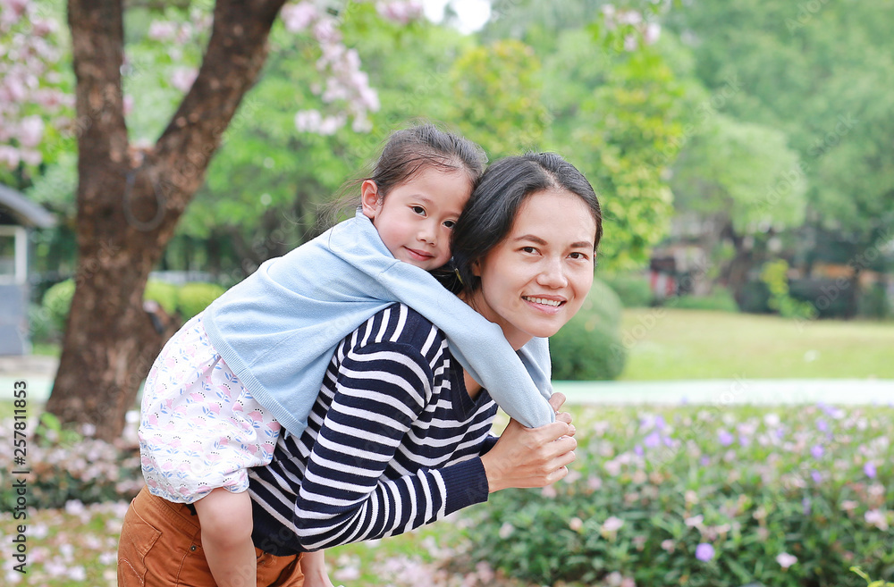 Happy mother carrying her daughter in garden with fully fall pink flower around. Happy loving family. Happy mother carrying her daughter in garden with fully fall pink flower around. Happy loving family.