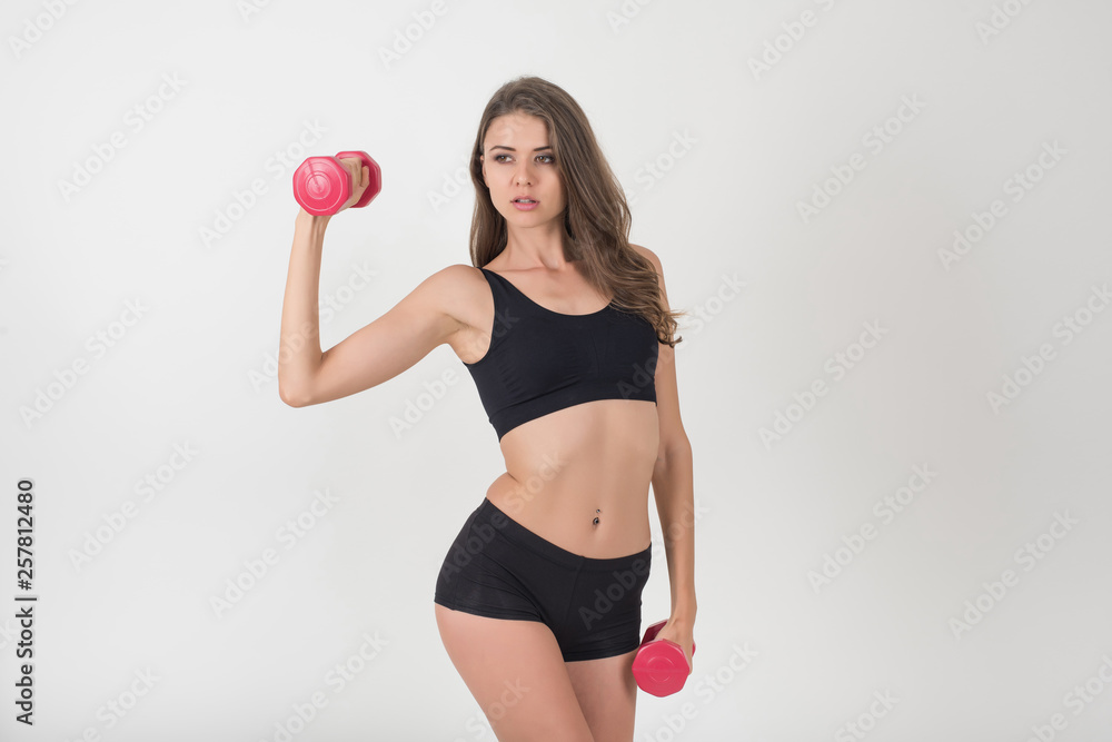 Fototapeta premium Portrait of young beautiful woman making physical exercises with dumbbells
