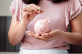 Close-Up Woman Hand is Putting a Money Coin into Piggy Bank on The Bedroom., Female Hand is Inserting Coin in Pink Piggy Saving. Business Banking and Financial Concept.
