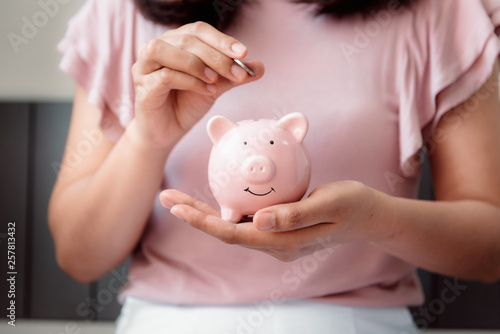 Close-Up Woman Hand is Putting a Money Coin into Piggy Bank on The Bedroom., Female Hand is Inserting Coin in Pink Piggy Saving. Business Banking and Financial Concept.
