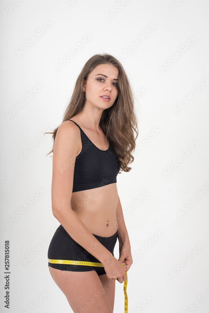 Obraz premium Portrait of beautiful young woman measuring her figure size with tape measure
