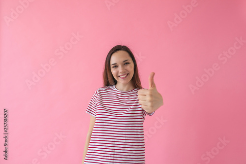 Positive smiling girl on a pink background shows fingers gesture meaning Like or Ok. © franz12