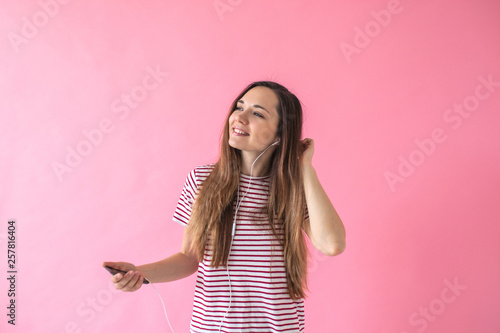 Positive joyful girl on a pink background listening to music. © franz12