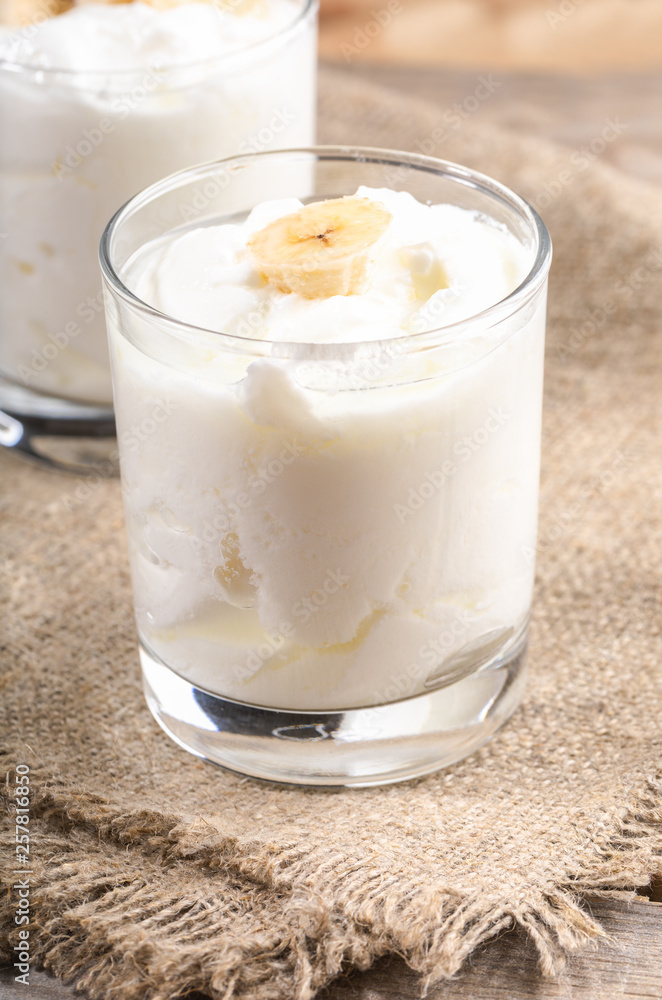 Traditional homemade yogurt with banana slices in transparent glasses on burlap napkin. Traditional homemade yogurt with banana slices in transparent glasses on burlap napkin.