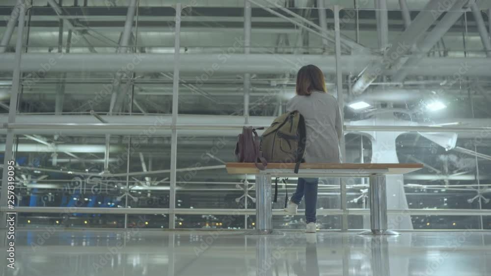 Happy Asian woman looking around sitting on chair in terminal hall while waiting her flight at the departure gate in international airport. Lifestyle women happy in airport concept. Happy Asian woman looking around sitting on chair in terminal hall while waiting her flight at the departure gate in international airport. Lifestyle women happy in airport concept.