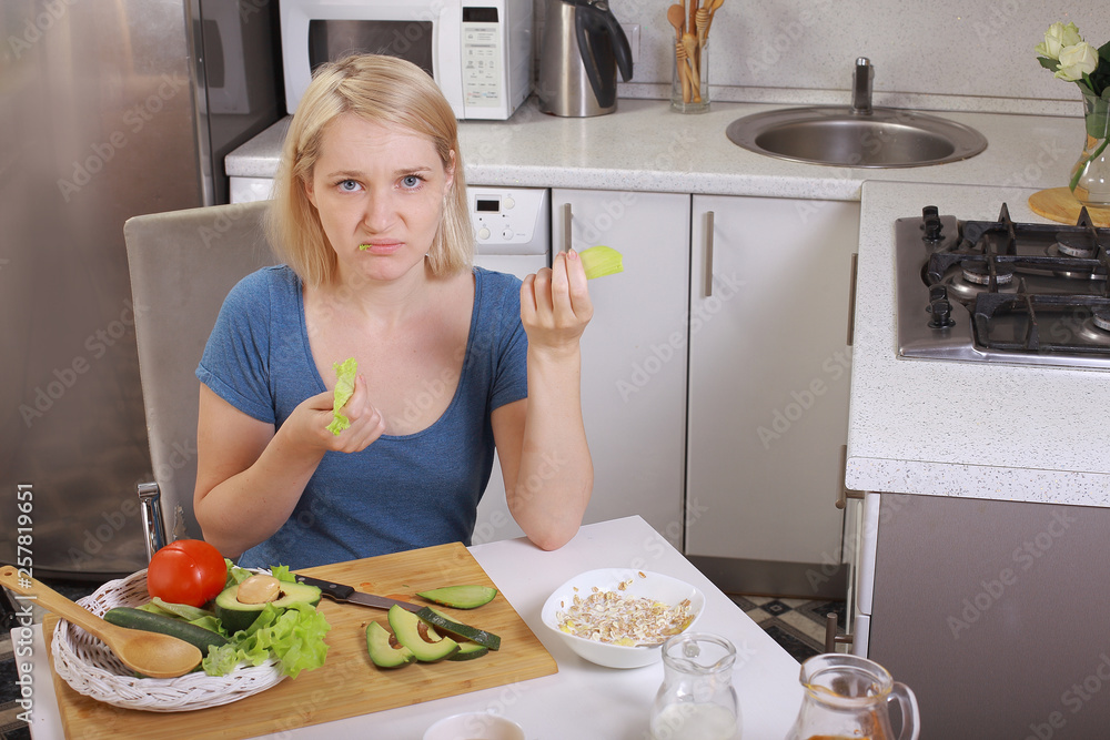 girl eating an avocado and salad, healthy eating, diet. pensive woman looks at the tomato. in the kitchen. bright room
