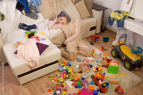Mother sitting on the couch. Mom tired to tidy up the house. Child scattered toys. Children's room. Mess in the house