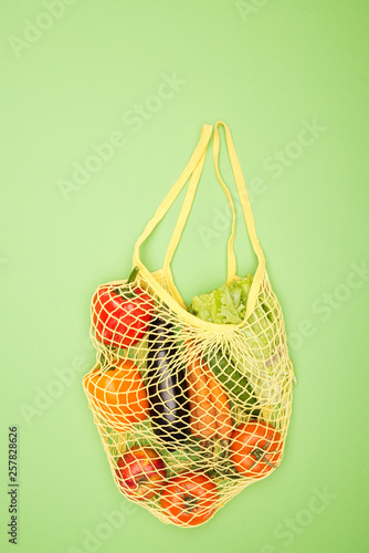 top view of yellow string bag with ripe organic vegetables on light green surface with copy space