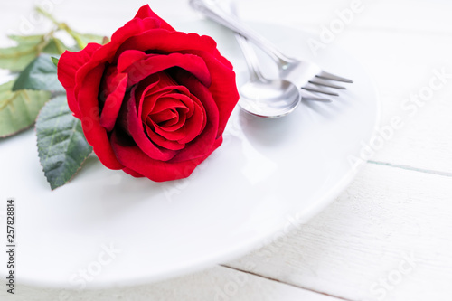 Red rose on white plate with spoon and fork on white painted wooden table