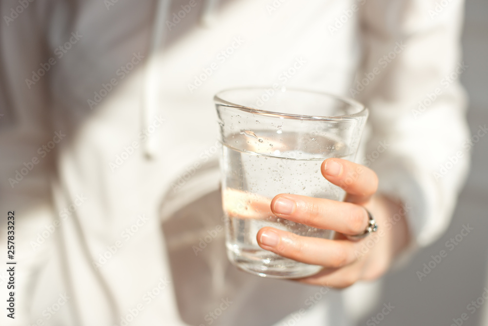 Close-up girl hands in the office stands in the sunlight holding a glass of clean water in between work Close-up girl hands in the office stands in the sunlight holding a glass of clean water in between work