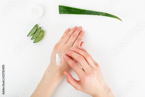 Opened plastic container with cream  sliced aloe vera plant and woman s hands on a white background