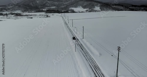 Aerial view of snow covered landscape with road and car