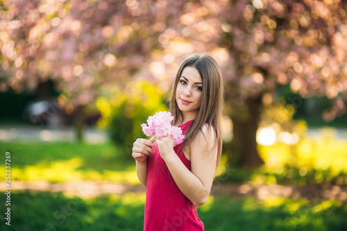 Portrait of charming girl in a fuchsia dress. She hold a flowers of sakura in her hands. Background of japanese tree