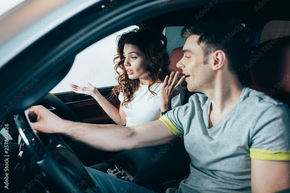 selective focus of curly woman gesturing while sitting near man in automobile selective focus of curly woman gesturing while sitting near man in automobile