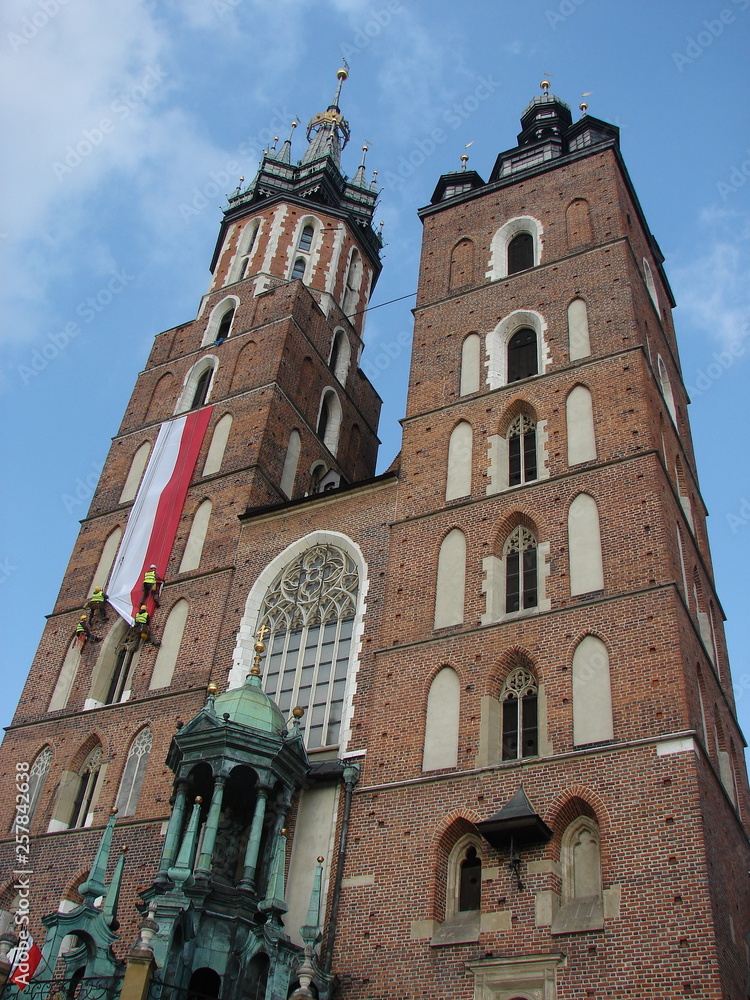 Big long national Polish flag hangs on tower of Saint Mary's Church in Krakow, poland, four men works with the flag, view from down