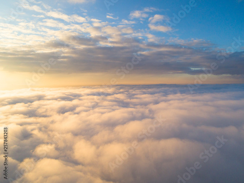 Aerial view White clouds in blue sky. Top view. View from drone. Aerial bird's eye view. Aerial top view cloudscape. Texture of clouds. View from above. Sunrise or sunset over clouds