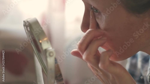Skin care concept. Woman middle age apply cream on face in front of mirror, close-up