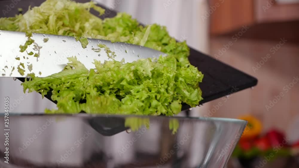 Woman hand swipe cut lettuce in slices into bowl from a cutting board - closeup, slow motion Woman hand swipe cut lettuce in slices into bowl from a cutting board - closeup, slow motion
