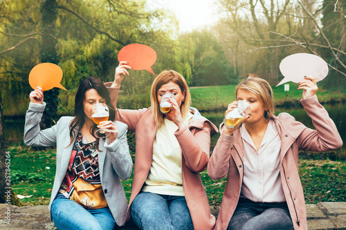 group of girls in the park drinking beer together while holding a thought bubble on their hands. Friendship and communication concept.