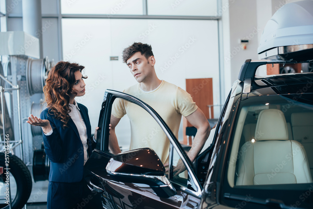 serious car dealer and handsome man standing near new car serious car dealer and handsome man standing near new car