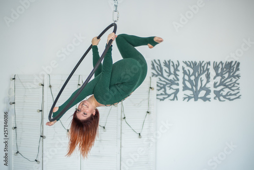 Beautiful and graceful aerial gymnast performs exercises on the air ring. Aerialist. Woman on aerial hoop photo